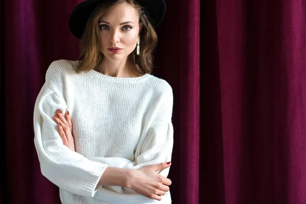 Ritratto di attraente donna bruna in cappello nero in piedi con le braccia incrociate e guardando la fotocamera — Foto stock