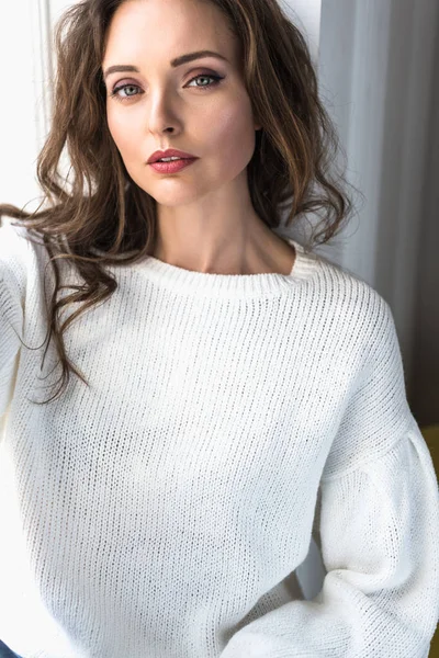 Porträt einer schönen jungen brünetten Frau im weißen Pullover, die in die Kamera blickt — Stockfoto