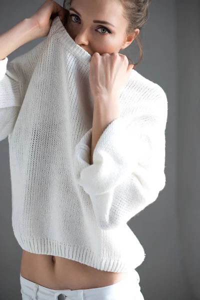Чувственная молодая женщина снимает белый свитер и смотрит в камеру на сером — стоковое фото