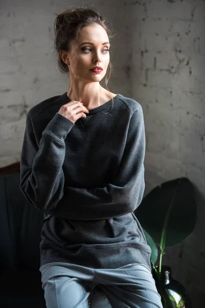 Retrato de la hermosa mujer morena en ropa gris de moda sentado en el sillón y mirando hacia otro lado - foto de stock