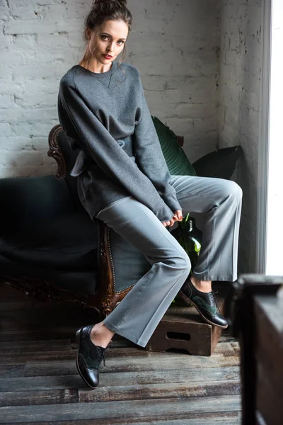 Schöne brünette Mädchen im trendigen Outfit sitzt auf einem Sessel und schaut in die Kamera — Stockfoto