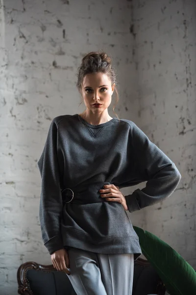 Retrato de hermosa mujer joven en jersey de moda con cinturón de pie con la mano en la cintura y mirando a la cámara - foto de stock