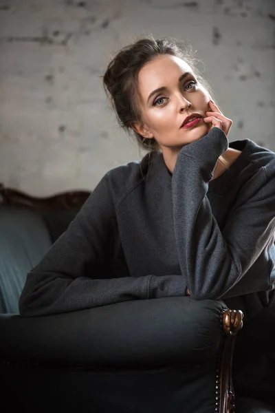 Attractive brunette woman in trendy jumper sitting on armchair and looking at camera — Stock Photo