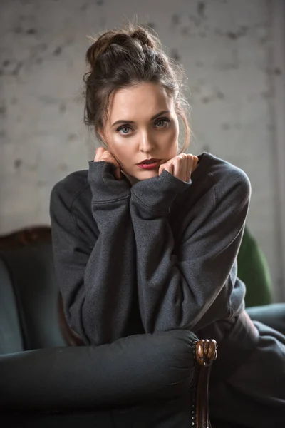 Retrato de bela mulher morena em camisola na moda sentado em poltrona e olhando para a câmera — Fotografia de Stock