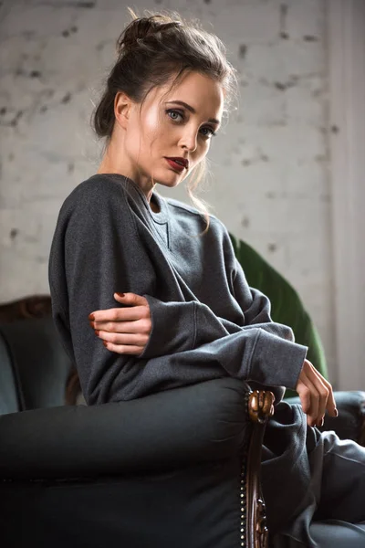 Portrait of beautiful young woman sitting on armchair and looking at camera — Stock Photo