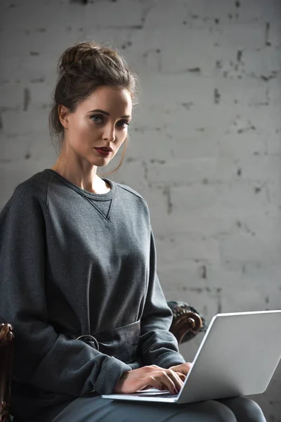 Beautiful brunette woman using laptop and looking at camera indoors — Stock Photo