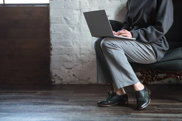 Cropped shot of girl in grey clothes and stylish shoes using laptop — Stock Photo