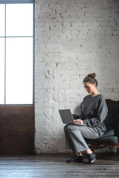 Vue pleine longueur de belle fille brune en utilisant un ordinateur portable à l'intérieur — Photo de stock