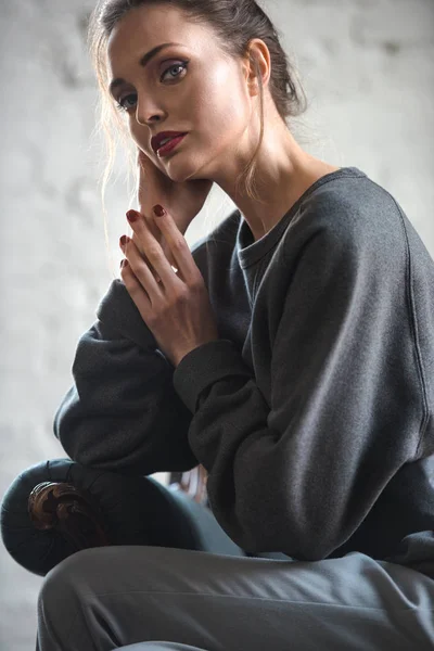 Belle femme brune en vêtements gris assis sur un fauteuil et regardant la caméra — Photo de stock