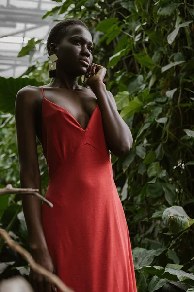 Attractive elegant african american girl posing in red dress in tropical garden — Stock Photo