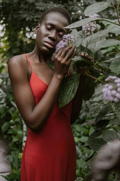 Chica afroamericana tierna de moda en vestido rojo posando con flores - foto de stock