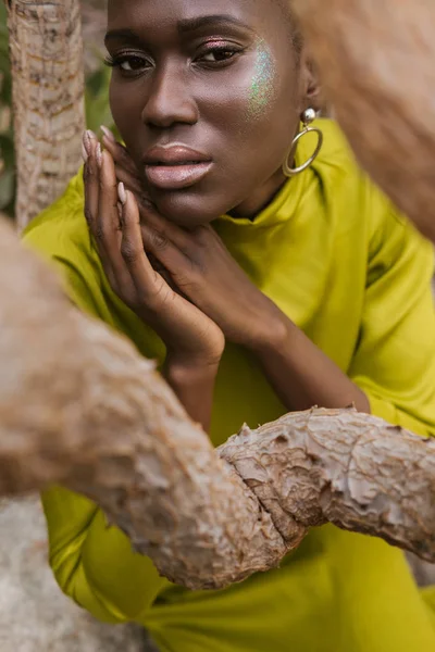 Séduisante femme afro-américaine avec un maquillage pailleté posant en robe jaune — Photo de stock