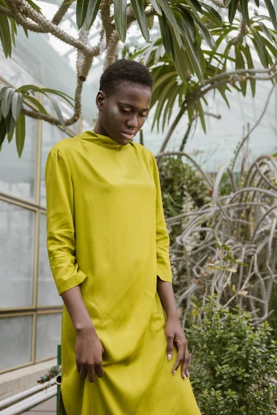 Stylish african american woman with glitter makeup posing in tropical glasshouse — Stock Photo