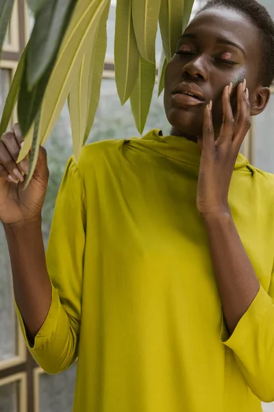 Atractiva chica afroamericana con estilo con maquillaje brillo posando en vestido amarillo - foto de stock