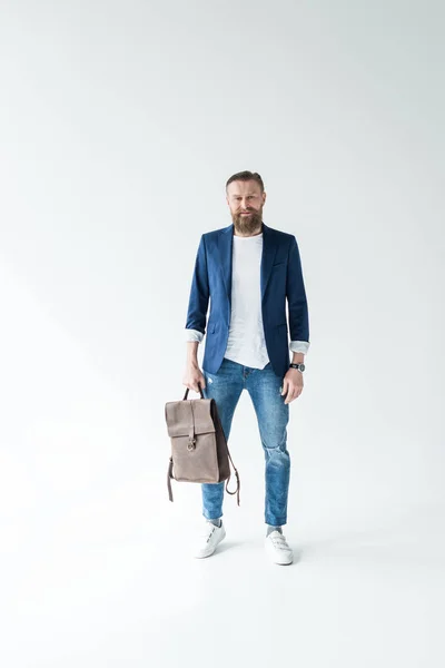 Stylish bearded man holding backpack on light background — Stock Photo