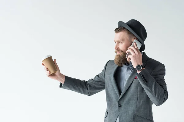 Empresário com bigode vintage e barba segurando copo de papel e falando no telefone isolado no fundo claro — Fotografia de Stock