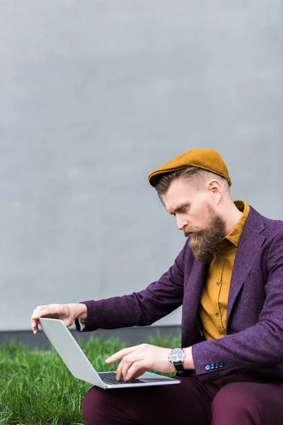 Businessman with vintage mustache and beard sitting on street and looking at laptop — Stock Photo