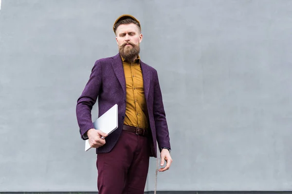 Homme d'affaires barbu élégant debout avec ordinateur portable — Photo de stock