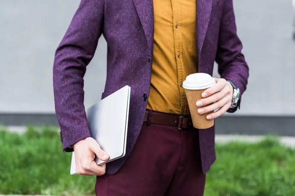 Cropped view of businessman holding laptop and paper cup — Stock Photo