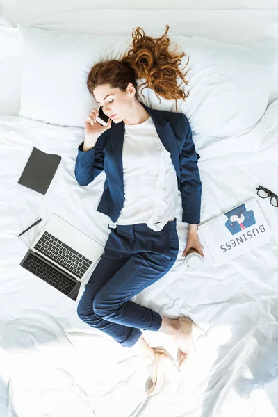 Vista superior de la mujer de negocios en traje hablando por teléfono en la cama entre carpetas y documentos - foto de stock