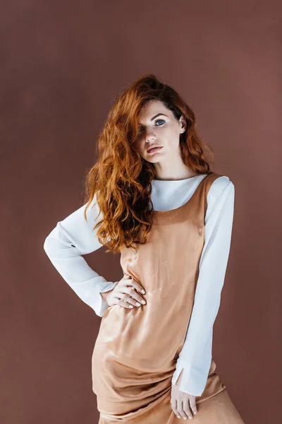 Atractiva pelirroja en vestido beige aislada sobre fondo marrón - foto de stock