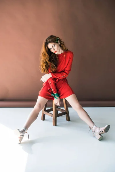 Donna con lunghi capelli rossi in abito rosso in posa su sgabello in legno — Foto stock