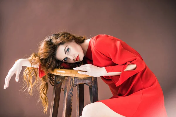 Woman with long red hair lying on wooden stool isolated on brown background — Stock Photo