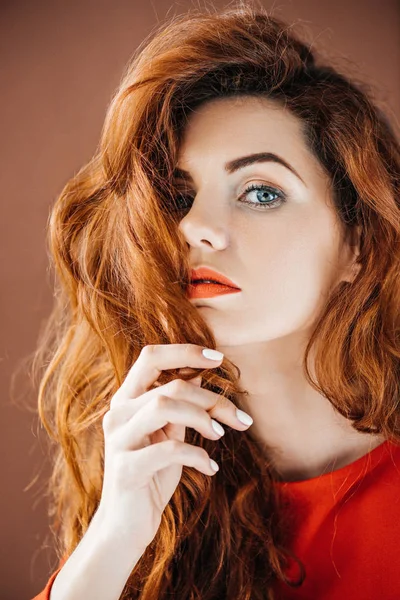 Привлекательная рыжая женщина касаясь волосы изолированы на коричневом фоне — стоковое фото