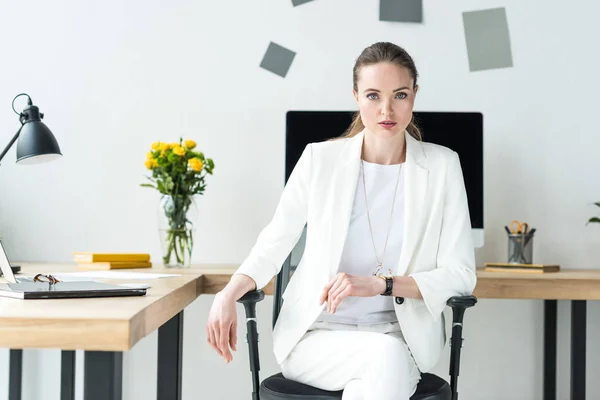 Portrait of beautiful businesswoman in white suit at workplace in office — Stock Photo