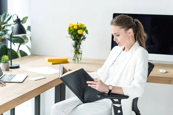 Вид збоку зосередженої бізнес-леді читання книги на робочому місці в офісі — стокове фото