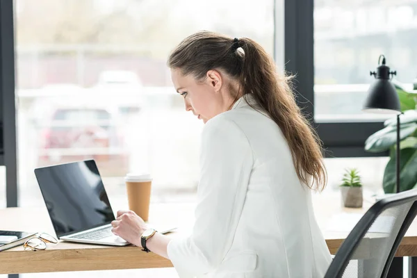 Боковой вид сосредоточенной бизнесвумен, работающей на ноутбуке на рабочем месте в офисе — стоковое фото