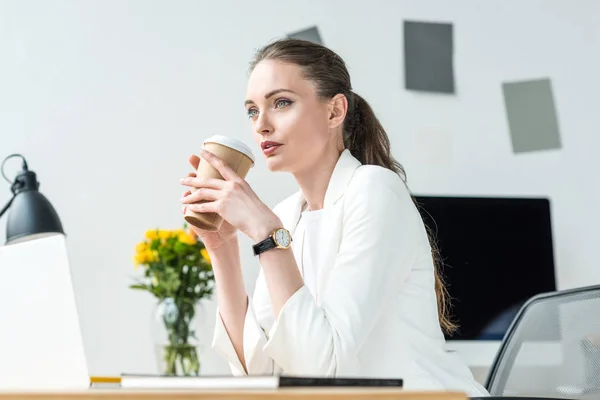 Side view of pensive businesswoman with coffee to go at workplace in office — Stock Photo