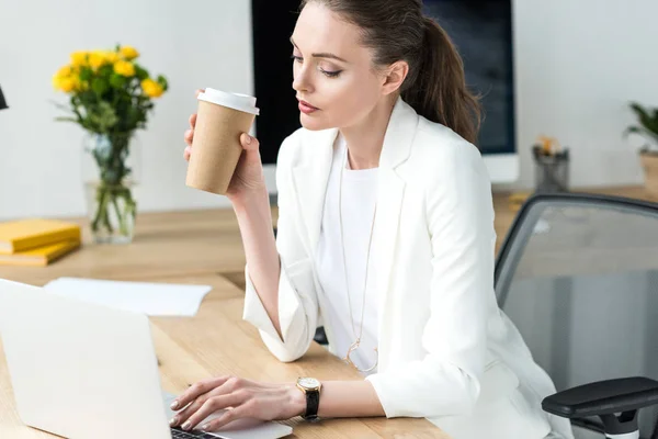 Mujer de negocios con café para ir a trabajar en el ordenador portátil en el lugar de trabajo en la oficina - foto de stock