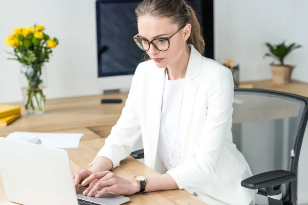 Donna d'affari concentrata in occhiali che lavorano su computer portatile a posto di lavoro in ufficio — Foto stock