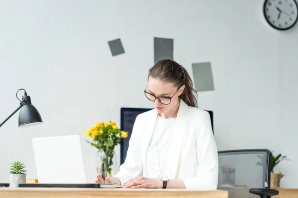 Porträt einer fokussierten Geschäftsfrau, die am Arbeitsplatz mit Laptop im Büro Papierkram erledigt — Stockfoto