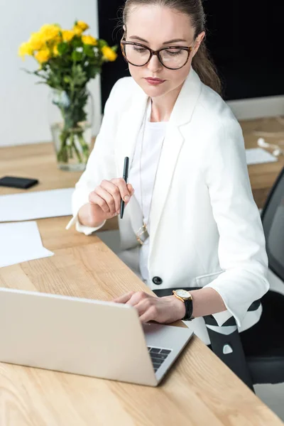 Porträt einer Geschäftsfrau mit Brille, die am Arbeitsplatz im Büro am Laptop tippt — Stockfoto