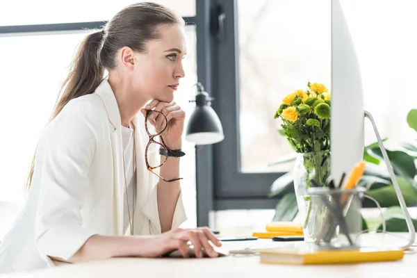 Seitenansicht einer fokussierten Geschäftsfrau, die am Arbeitsplatz im Büro auf den Computerbildschirm blickt — Stockfoto