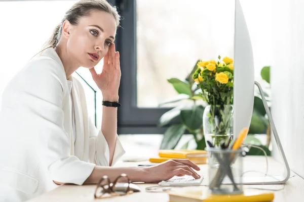 Side view of pensive businesswoman at workplace with computer screen in office — Stock Photo