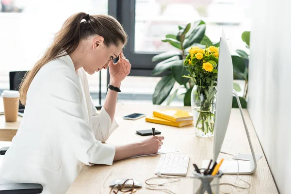 Вид збоку бізнес-леді робить нотатки на робочому місці з екраном комп'ютера в офісі — стокове фото