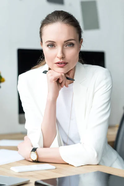 Retrato de hermosa mujer de negocios con pluma mirando a la cámara en el lugar de trabajo en la oficina - foto de stock