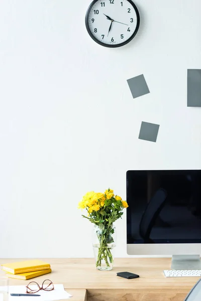 Vista de cerca del lugar de trabajo vacío con pantalla de computadora en blanco, ramo de flores de crisantemo y anteojos en la oficina - foto de stock