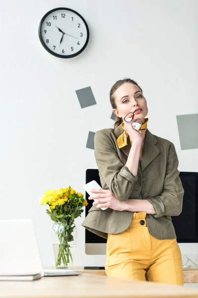 Atractiva mujer de negocios elegante con gafas y teléfono inteligente, mirando a la cámara en la oficina — Stock Photo