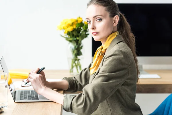 Beautiful stylish businesswoman looking at camera while working with laptop in office — Stock Photo