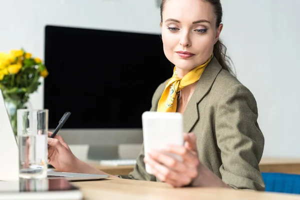 Beautiful smiling middle aged businesswoman using smartphone at workplace — Stock Photo