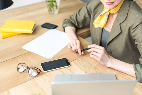 Recortado tiro de elegante mujer de negocios celebración de pluma y mirando a la computadora portátil en la oficina - foto de stock