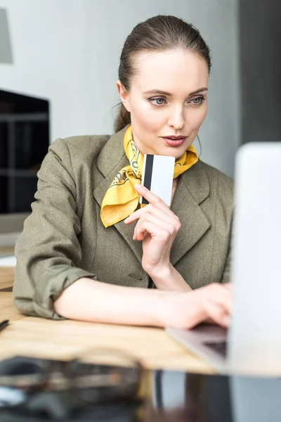 Femme d'affaires souriante tenant une carte de crédit et utilisant un ordinateur portable sur le lieu de travail — Photo de stock