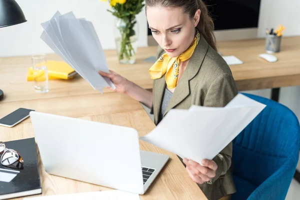 Высокий угол зрения красивой стильной деловой женщины с бумагами и глядя на ноутбук в офисе — стоковое фото