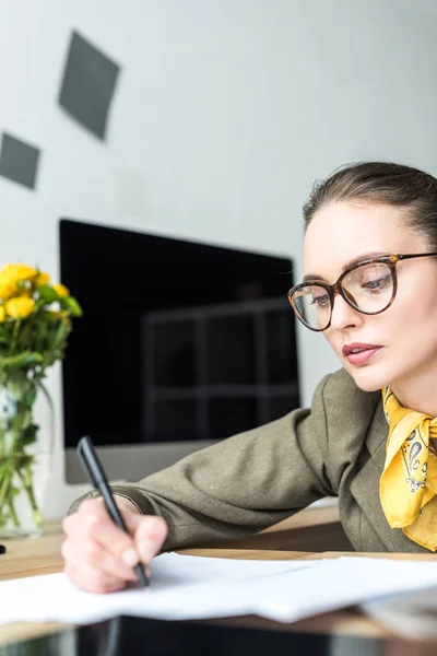 Hermosa mujer de negocios en gafas tomando notas en el lugar de trabajo - foto de stock