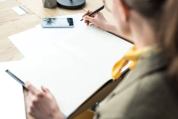 Selective focus of businesswoman in eyeglasses taking notes at workplace — Stock Photo