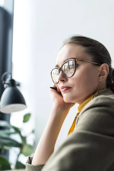 Bela empresária pensativa em óculos olhando para longe no local de trabalho — Fotografia de Stock